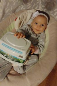 baby girl sitting in a bouncer seat with the container of baby formula