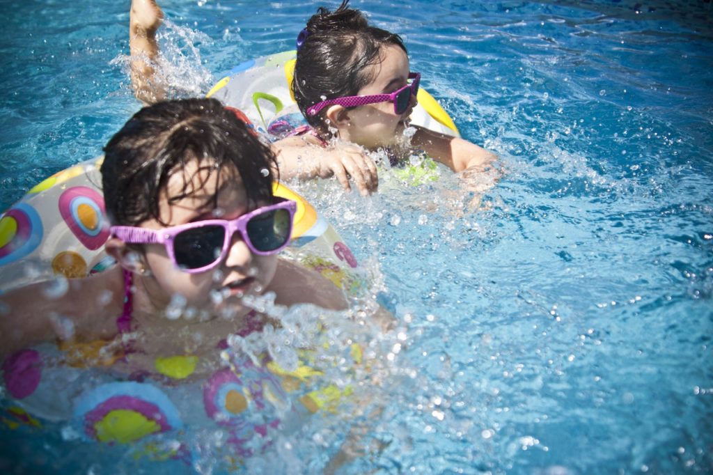 two little girls wearing sunglasses swimming in a clear blue pool.