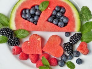 a slice of watermelon with hearts cut out of them, and blueberries filling the space on a white plate with the watermelon hearts and raspberries', blackberries, and blueberries on the plate