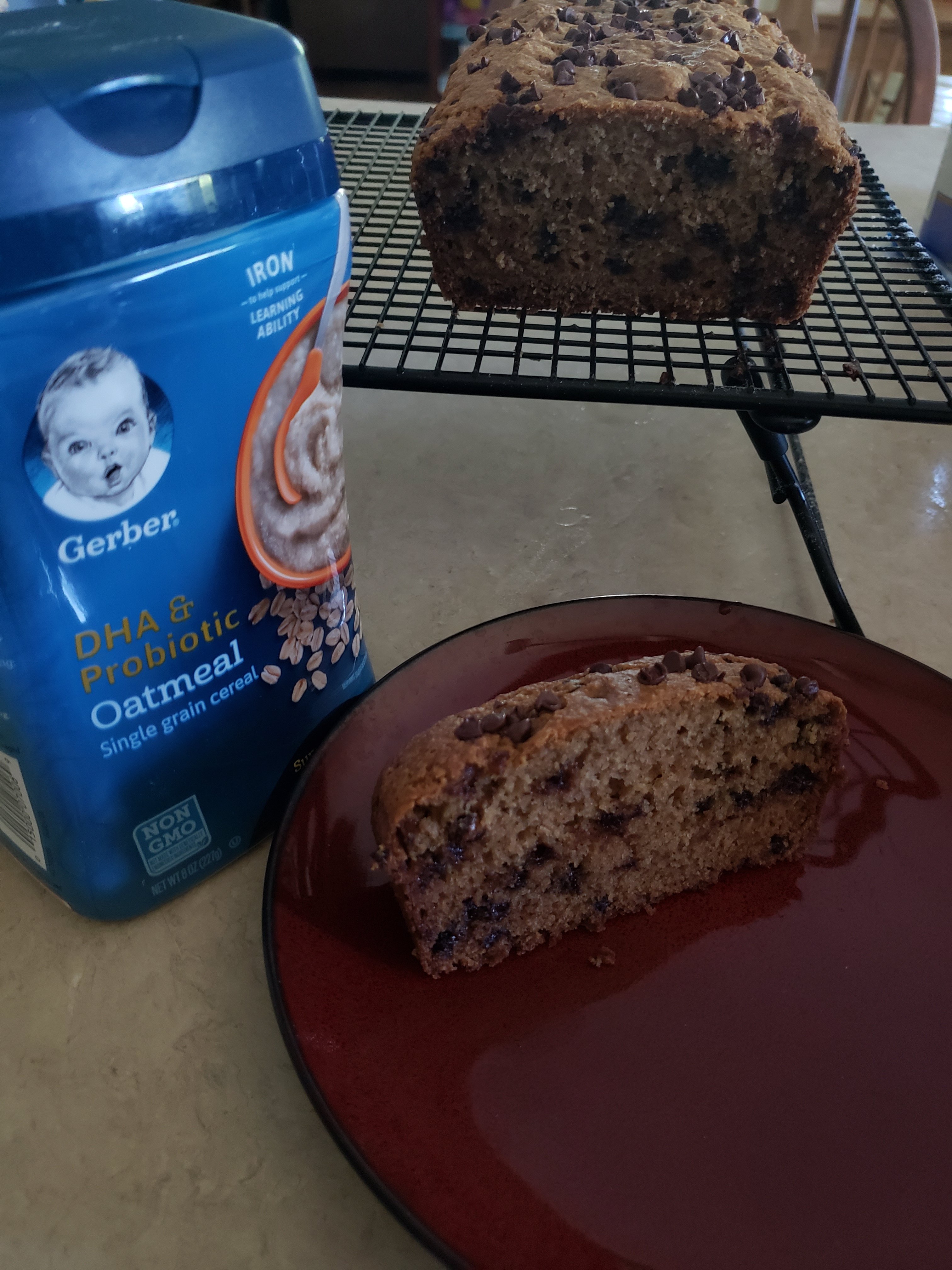 Chocolate Chip Oatmeal Quickbread with a piece cut off on a plate, a container of Gerber oatmeal cereal sitting beside the plate.