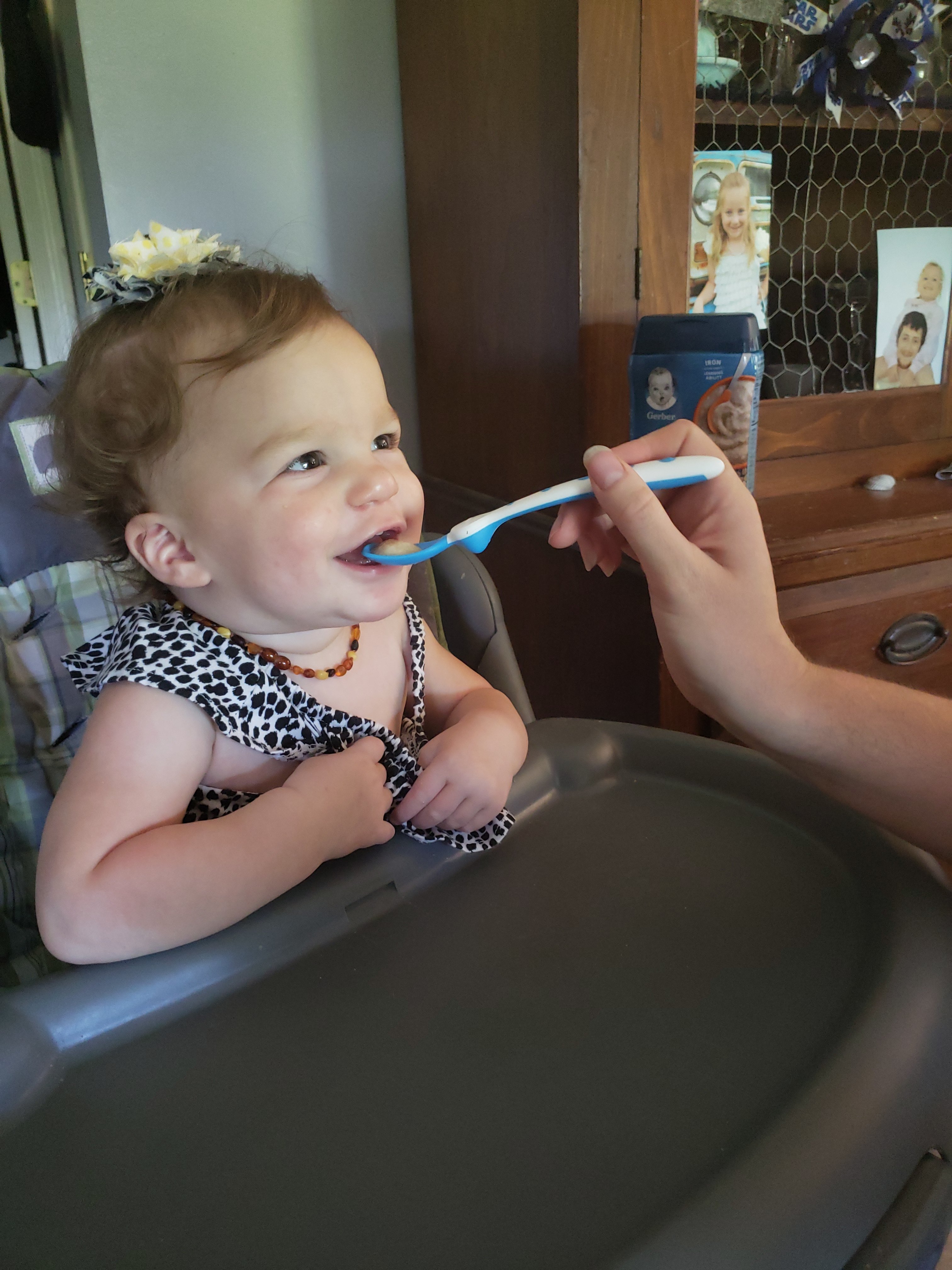 a baby girl sitting in a highchair being spoon fed Gerber cereal