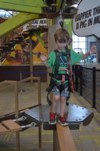 little boy in a safety harness about to walk across a balance beam