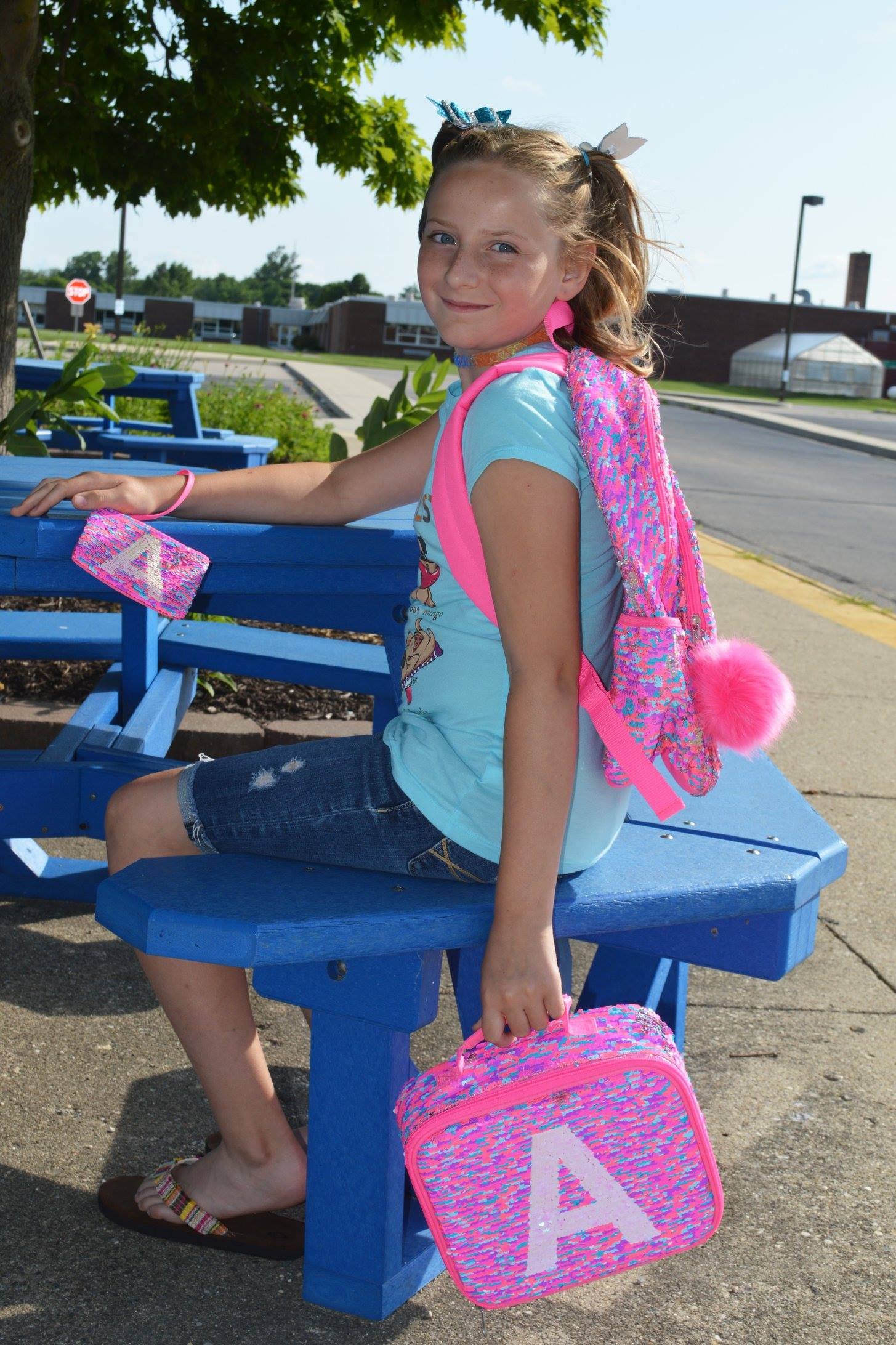 preteen girl with a pink backpack sitting at a picnic table smiling at the camera