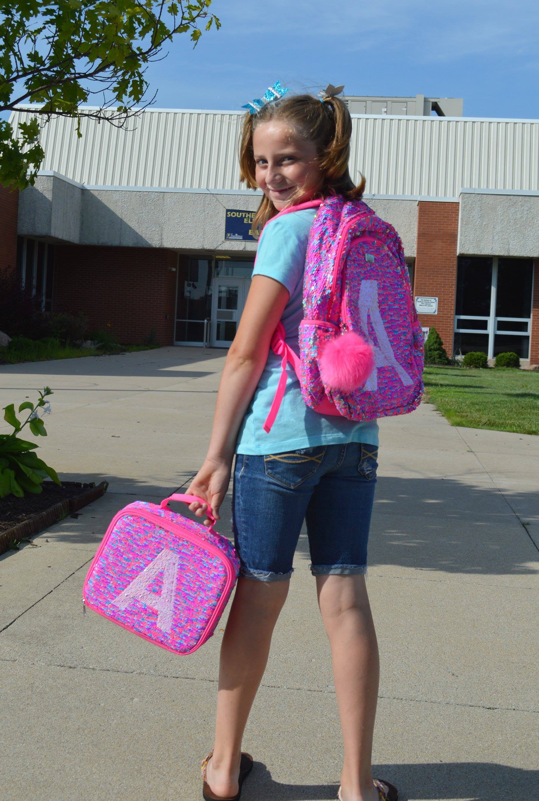 preteen girl with a sprinkle backpack and the letter A on it walking towards a school