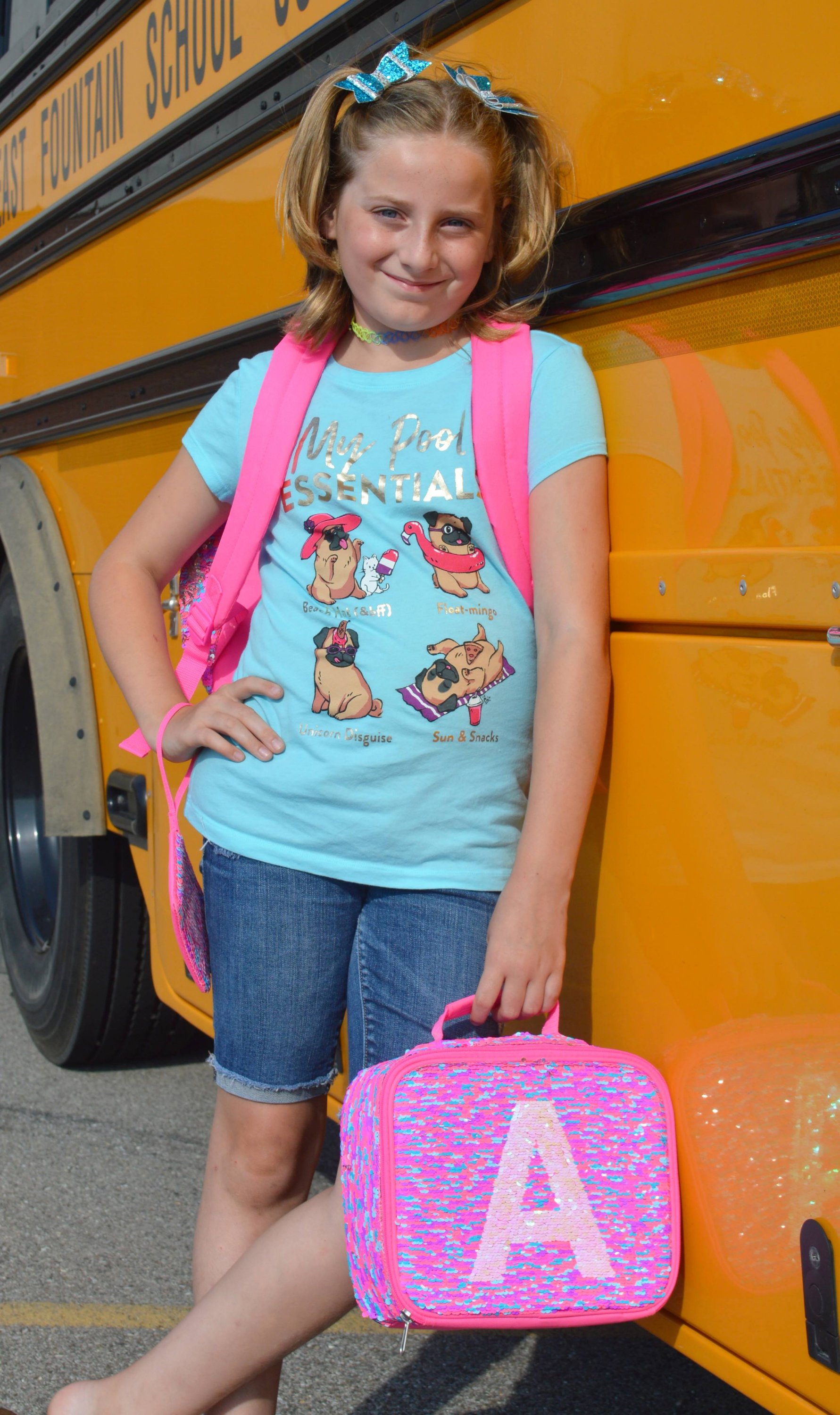 preteen girl wearing a pink backpack leaning against a school bus