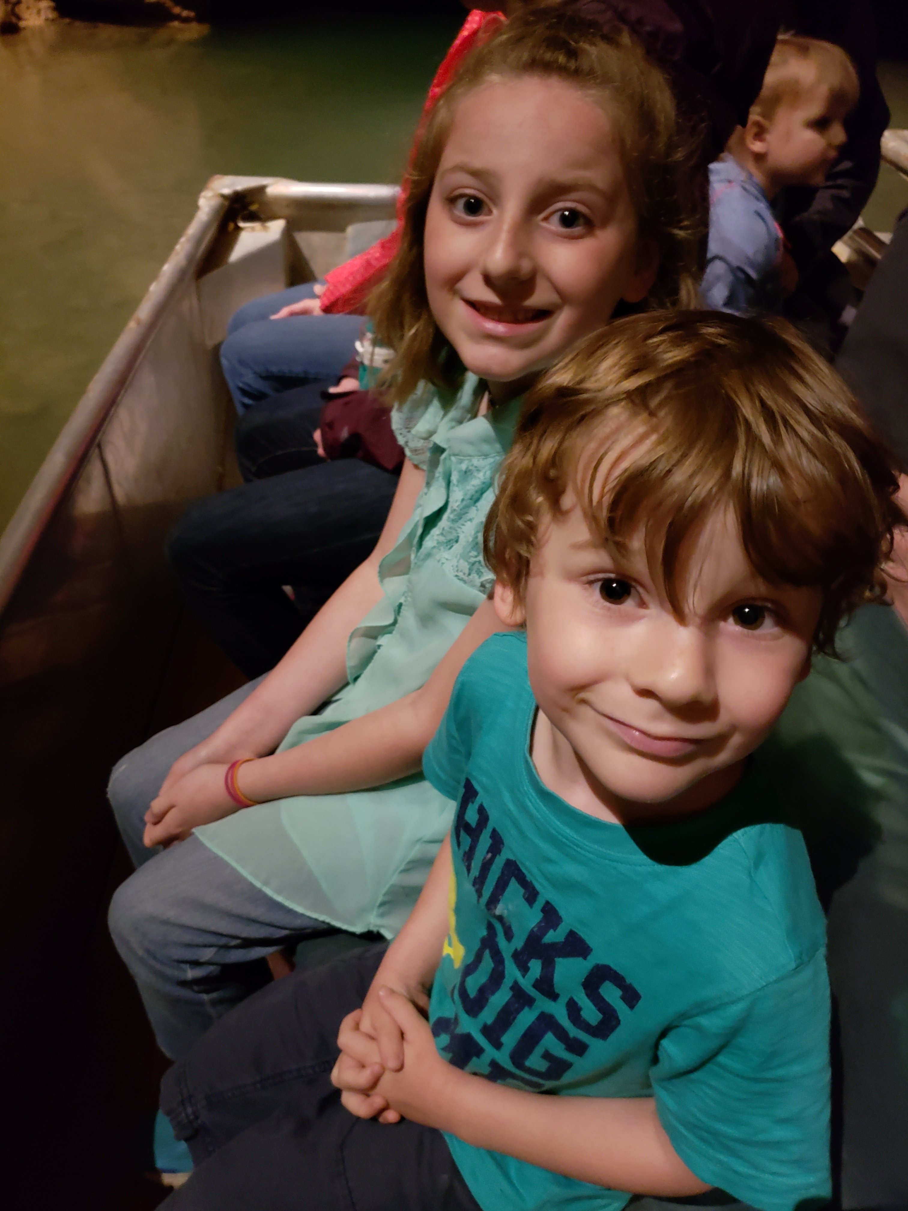 Two children, a boy and a girl, smiling at the camera while riding a boat through an underground river at Bluespring Caverns tour