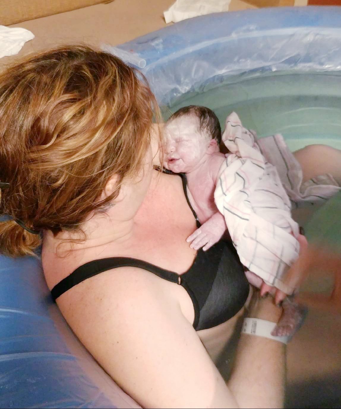 woman in birthing pool with newborn on her chest