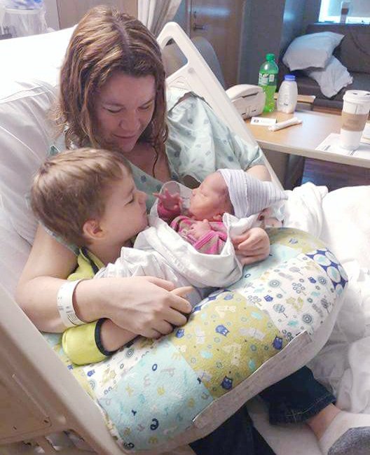 woman in hospital bed with a toddler holding a newborn baby