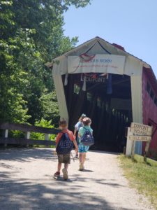 three kids walking towards a covered bridge 