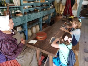 children sitting at a table with a women in period clothing replicating children learning at home