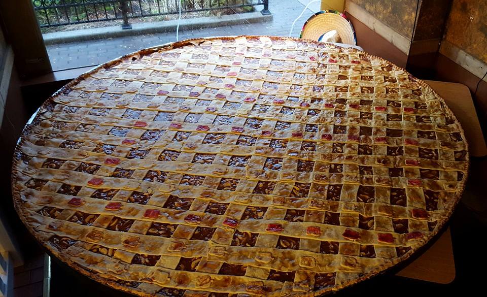  a very large, round pie on a table in front of a window