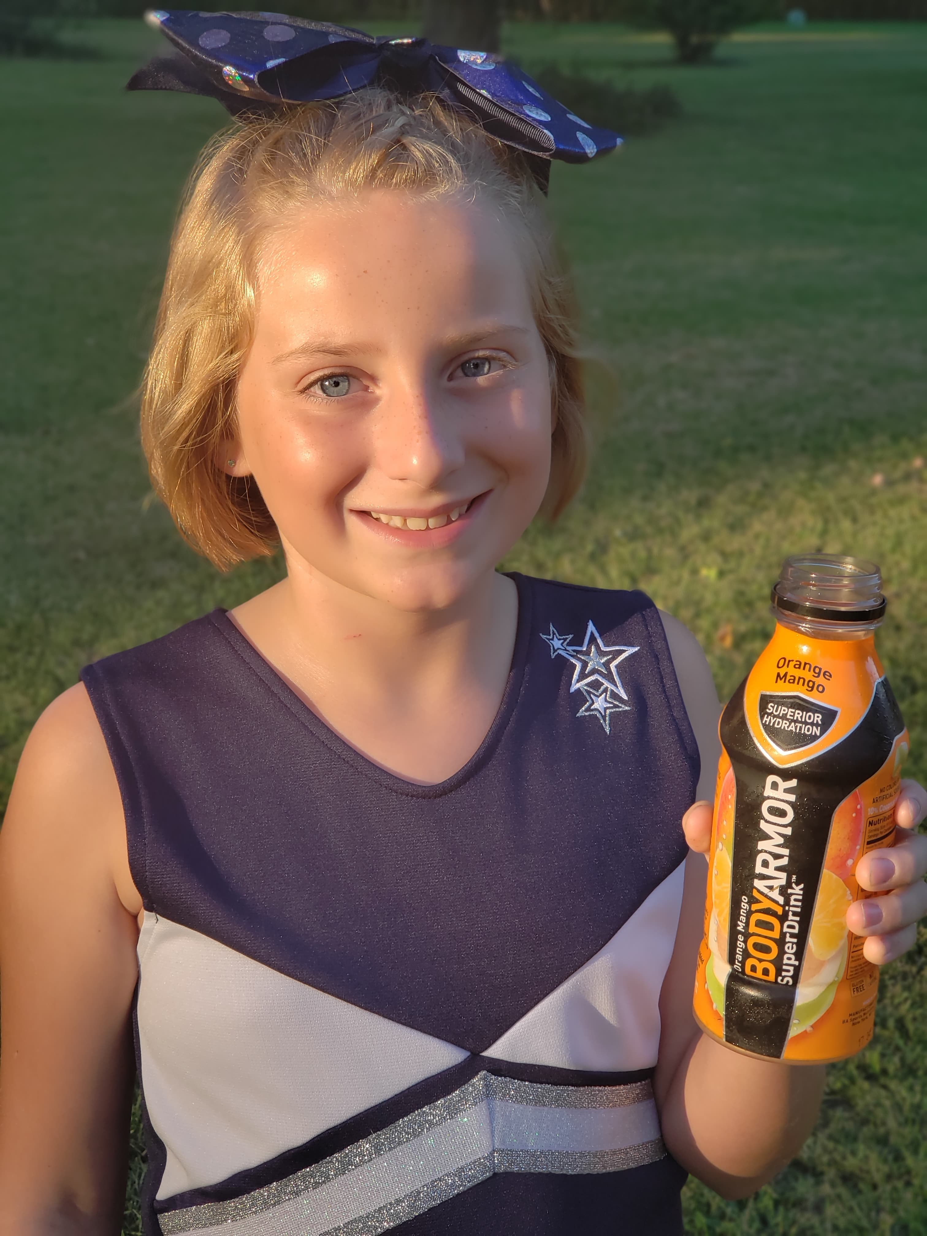 teen cheerleader standing outside holding a bottle of BodyAmor SuperDrink