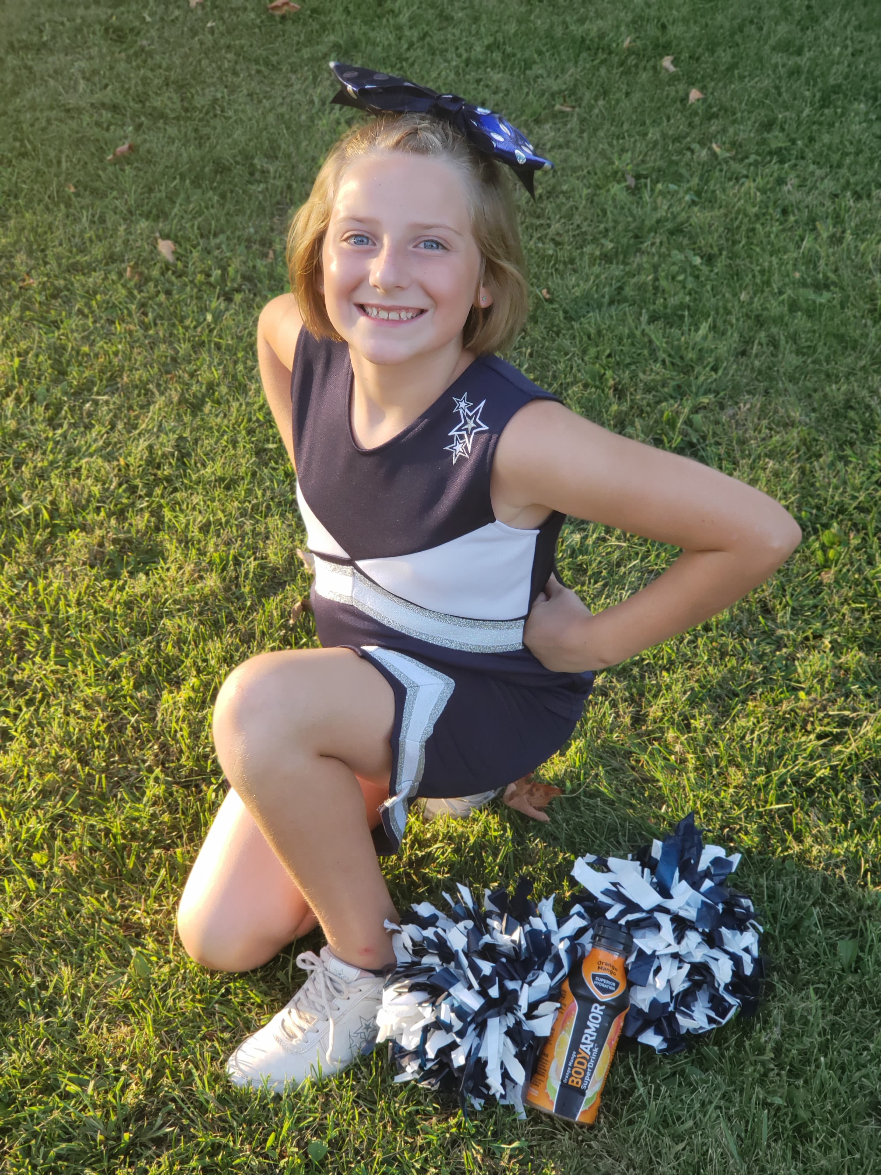 teen cheerleader kneeling outside next to a bottle of BodyAmor SuperDrink