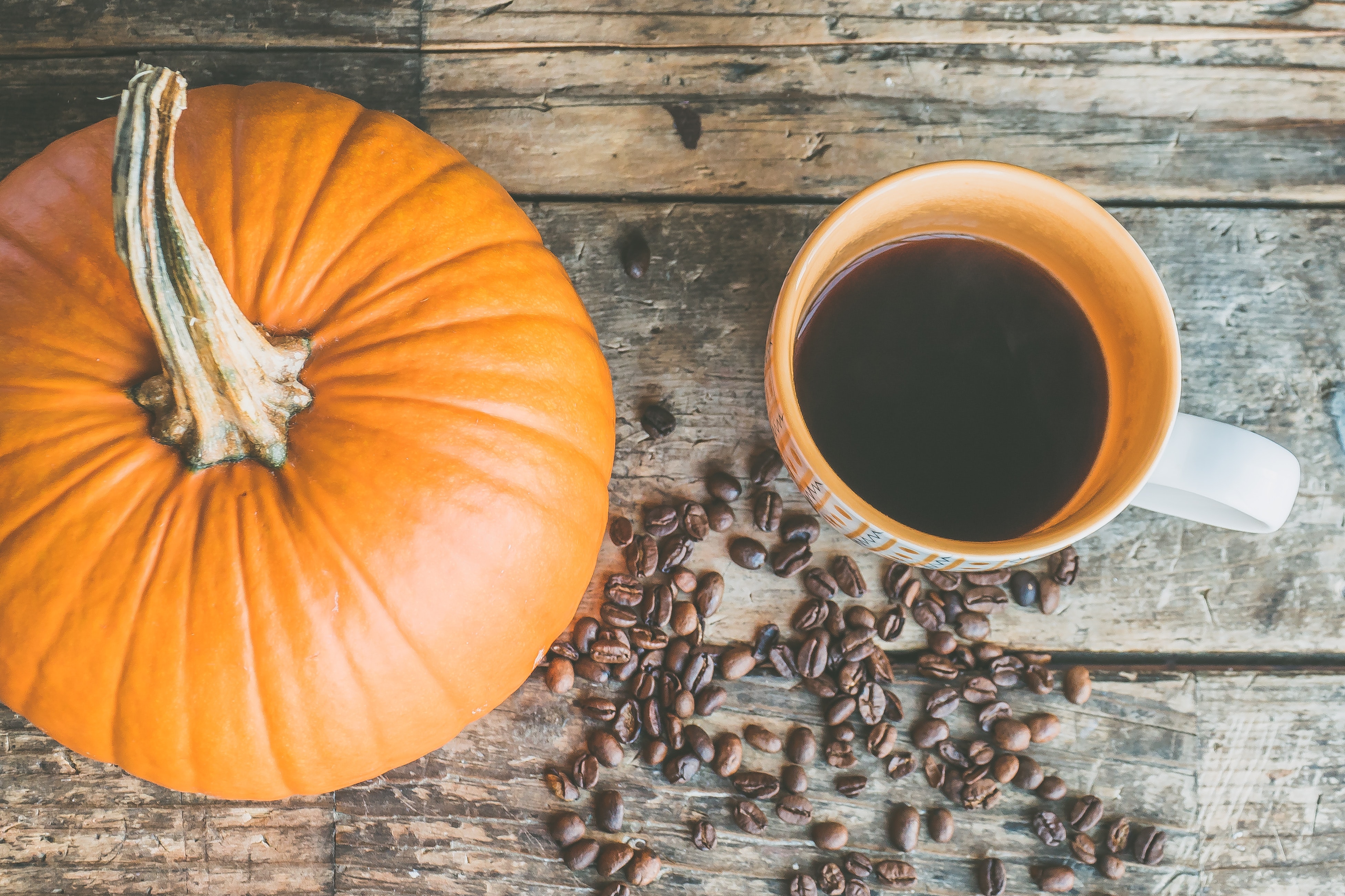 looking down at a small pumpkin, a cup of coffee with some coffee beans on the table around them