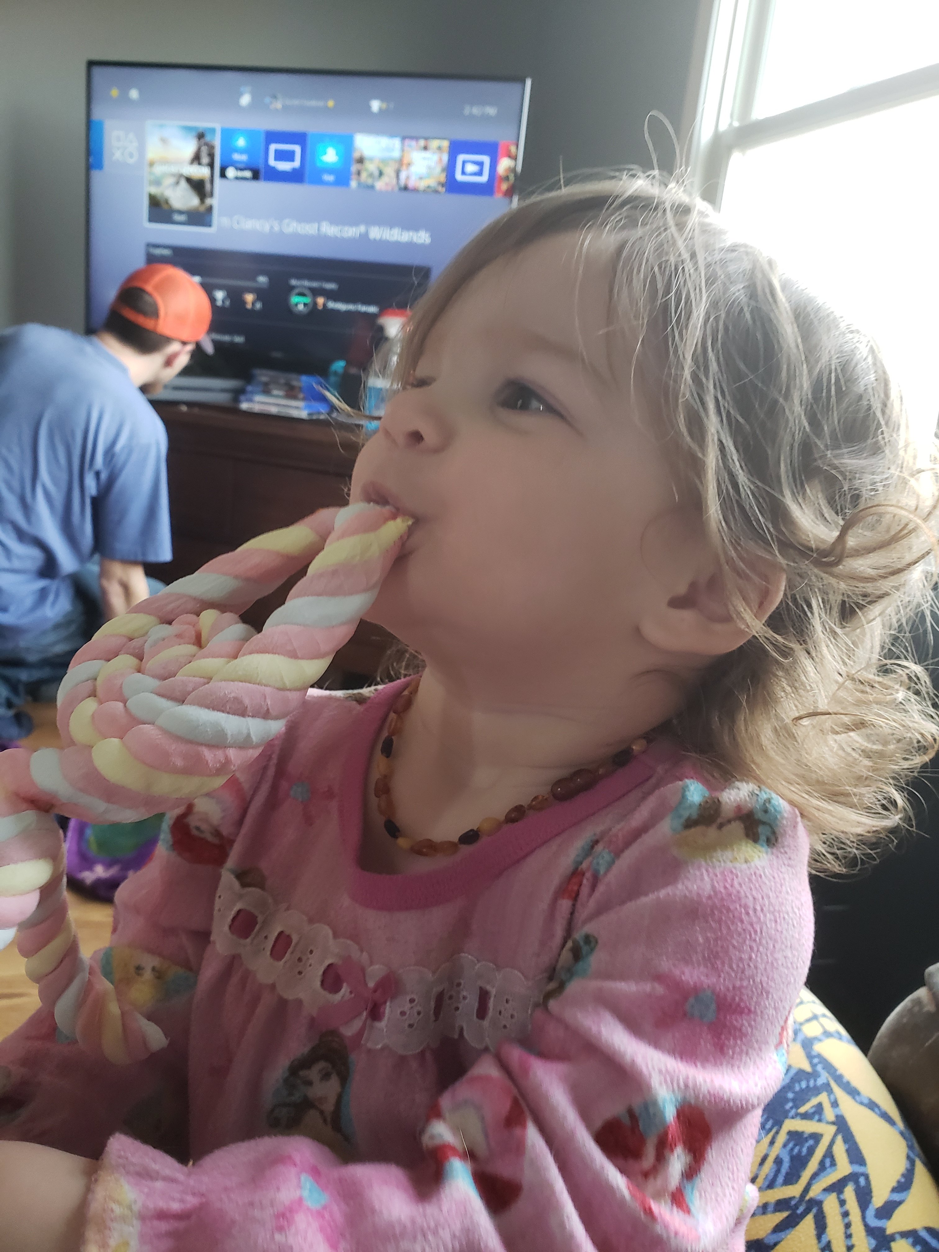 toddler girls eating marshmallow treat with man in background looking at TV