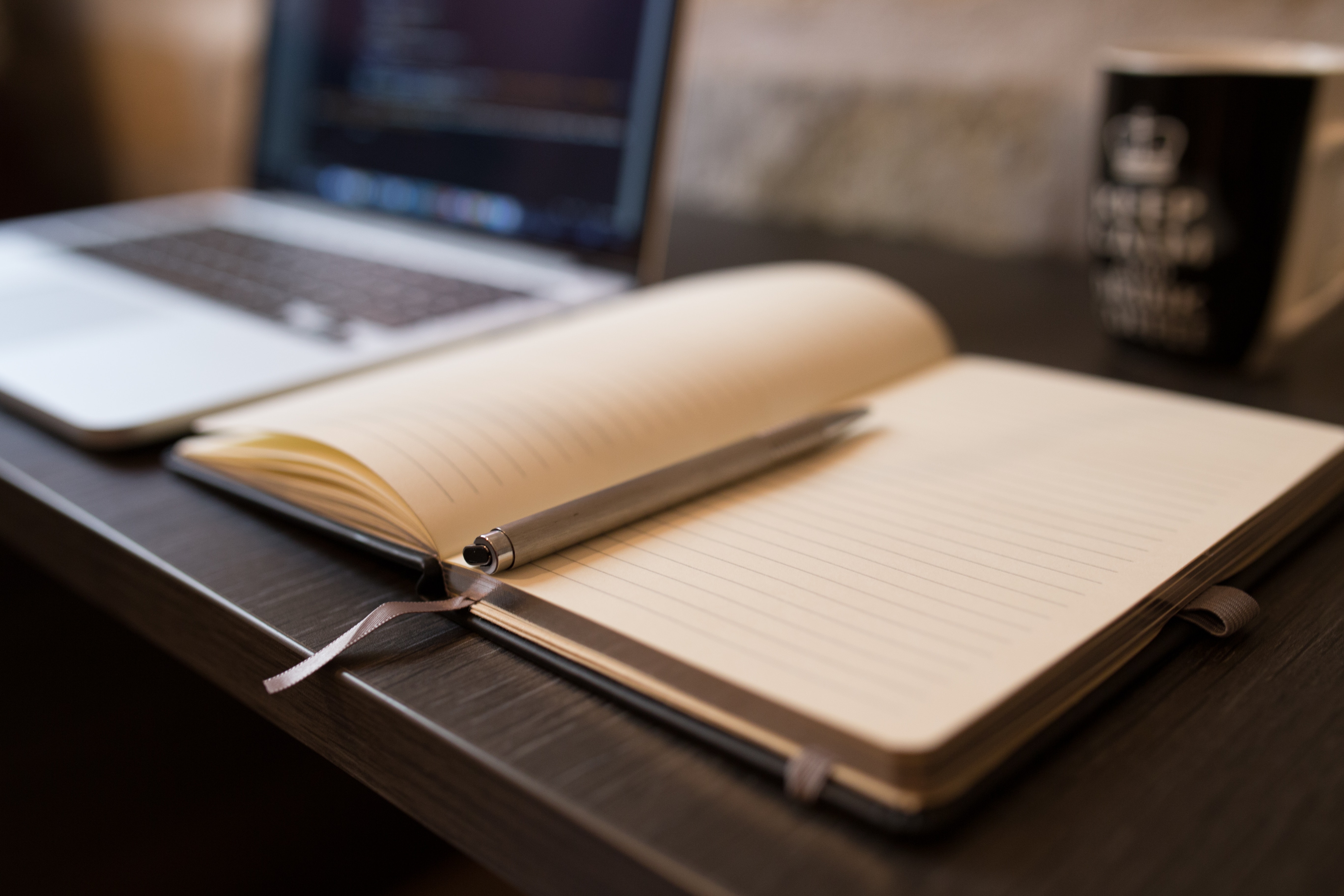 and open notebook with a pen on it sitting beside an open laptop