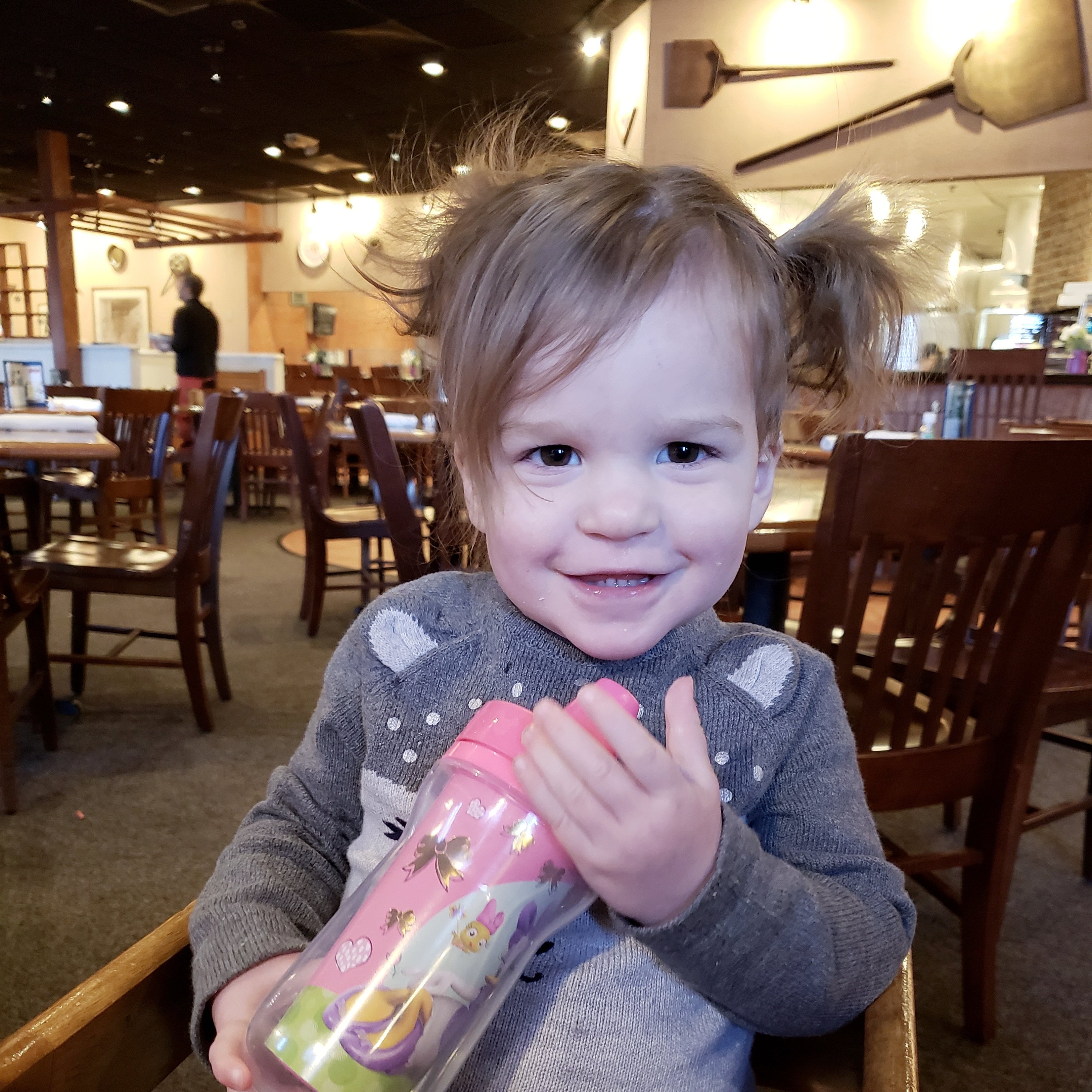 toddler girl sitting in a highchair holding a sippy cup in a restaurant