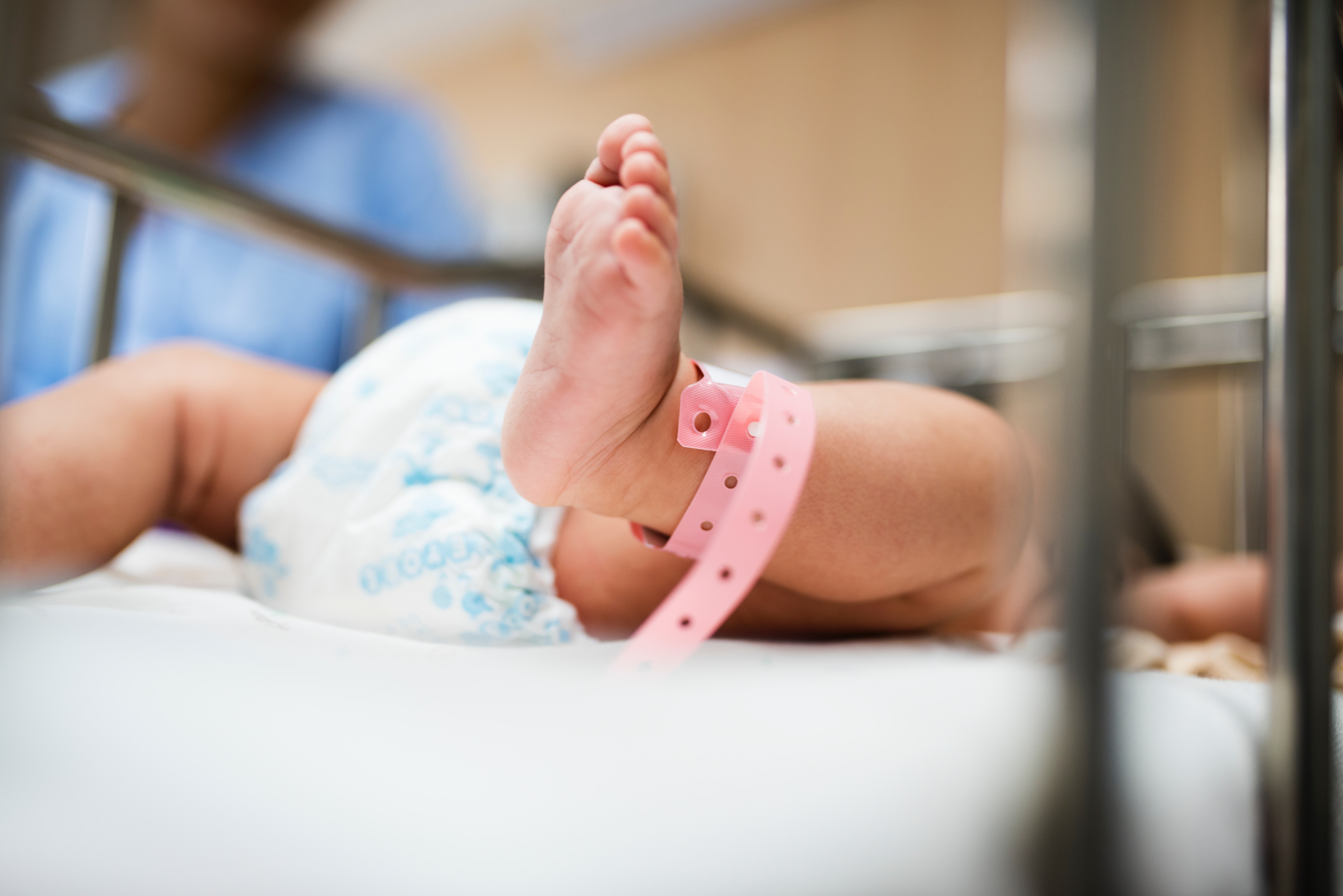 newborn in hospital bassinet with a pink ankle bracelet