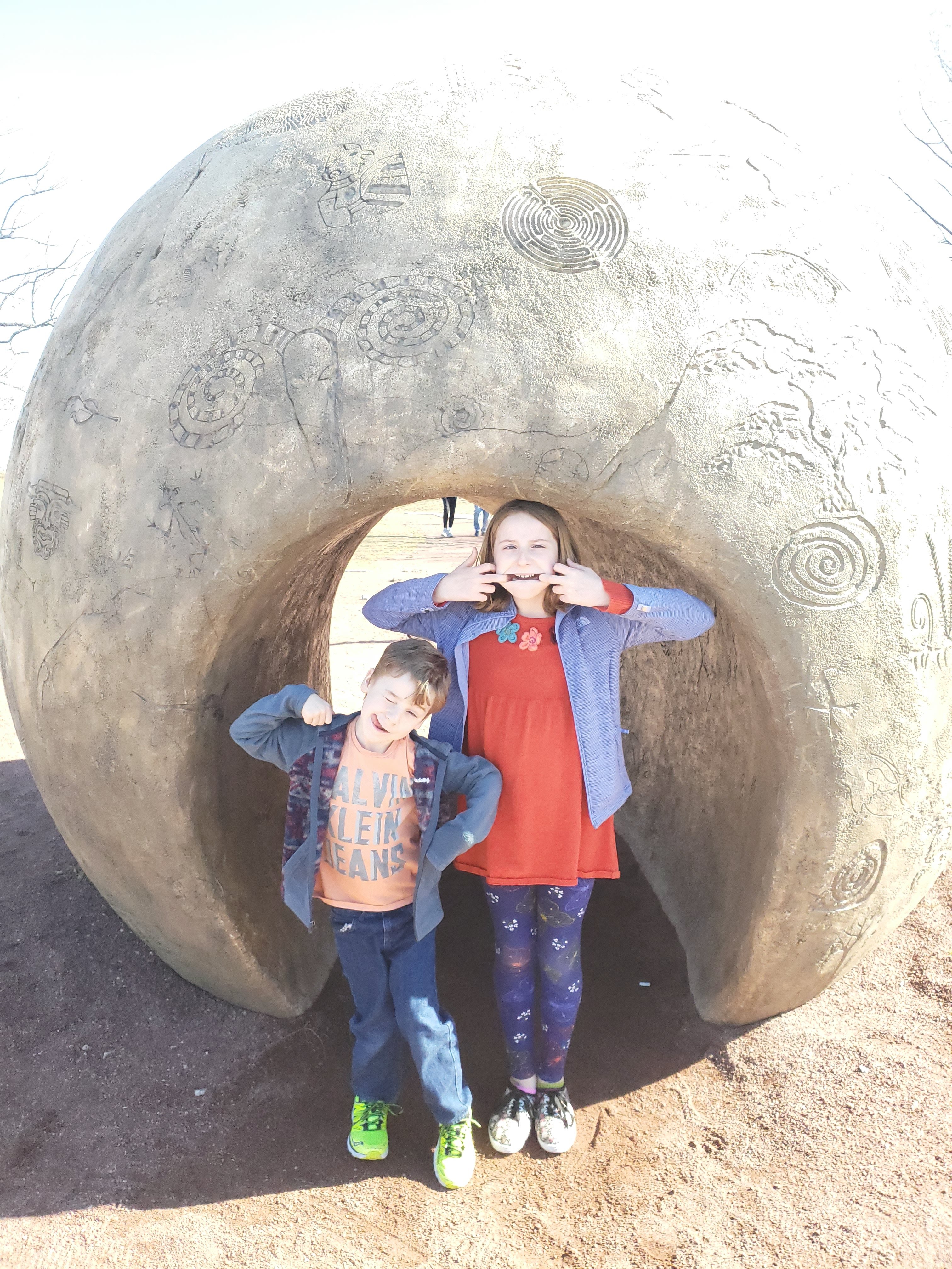 preteen girl and boy outside standing in front of a rock making silly faces