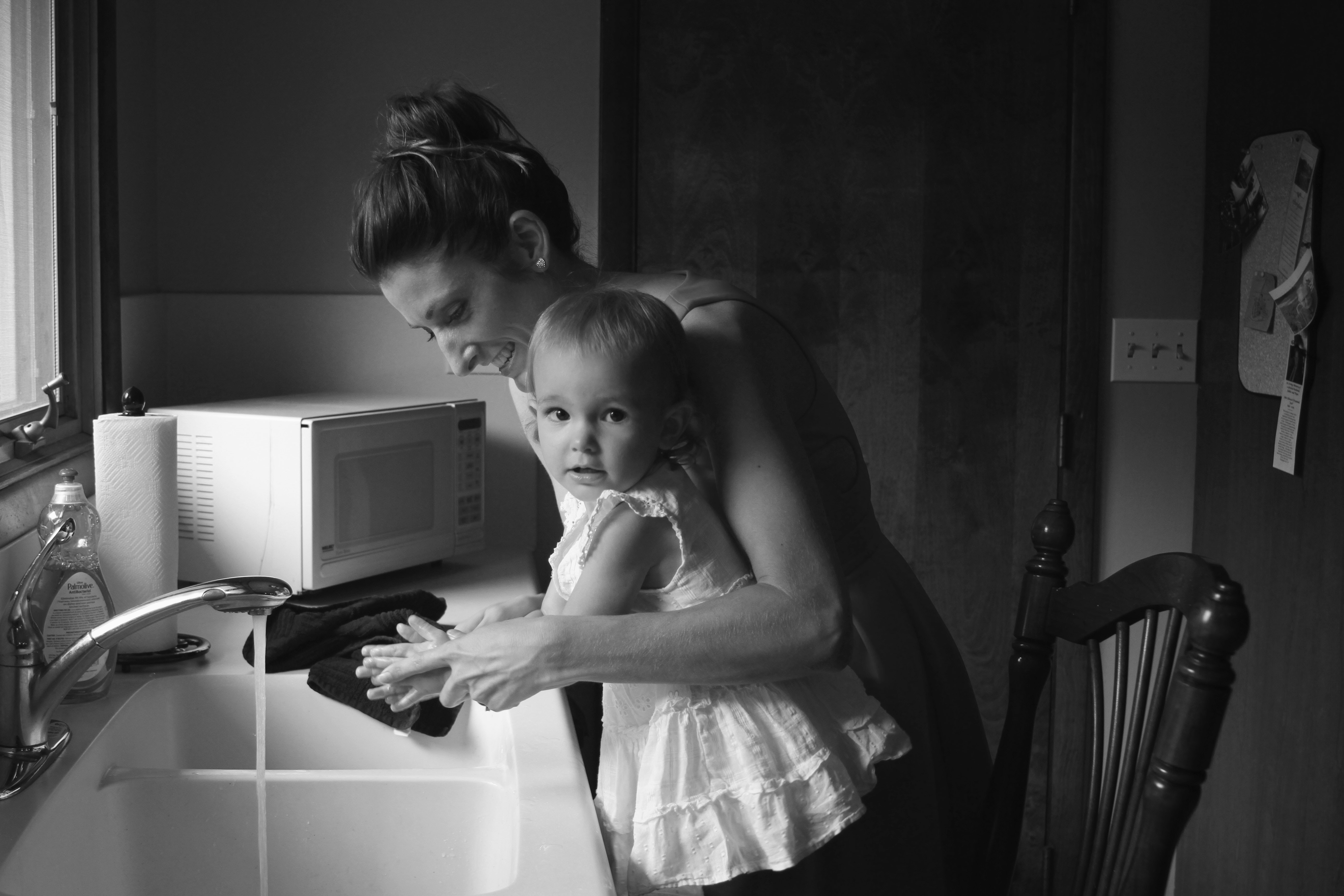 a woman standing at a kitchen with a toddler on a chair working on hand washing