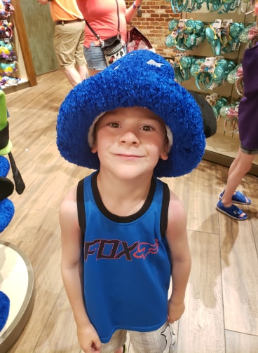 young boy wearing a silly blue hat in a store