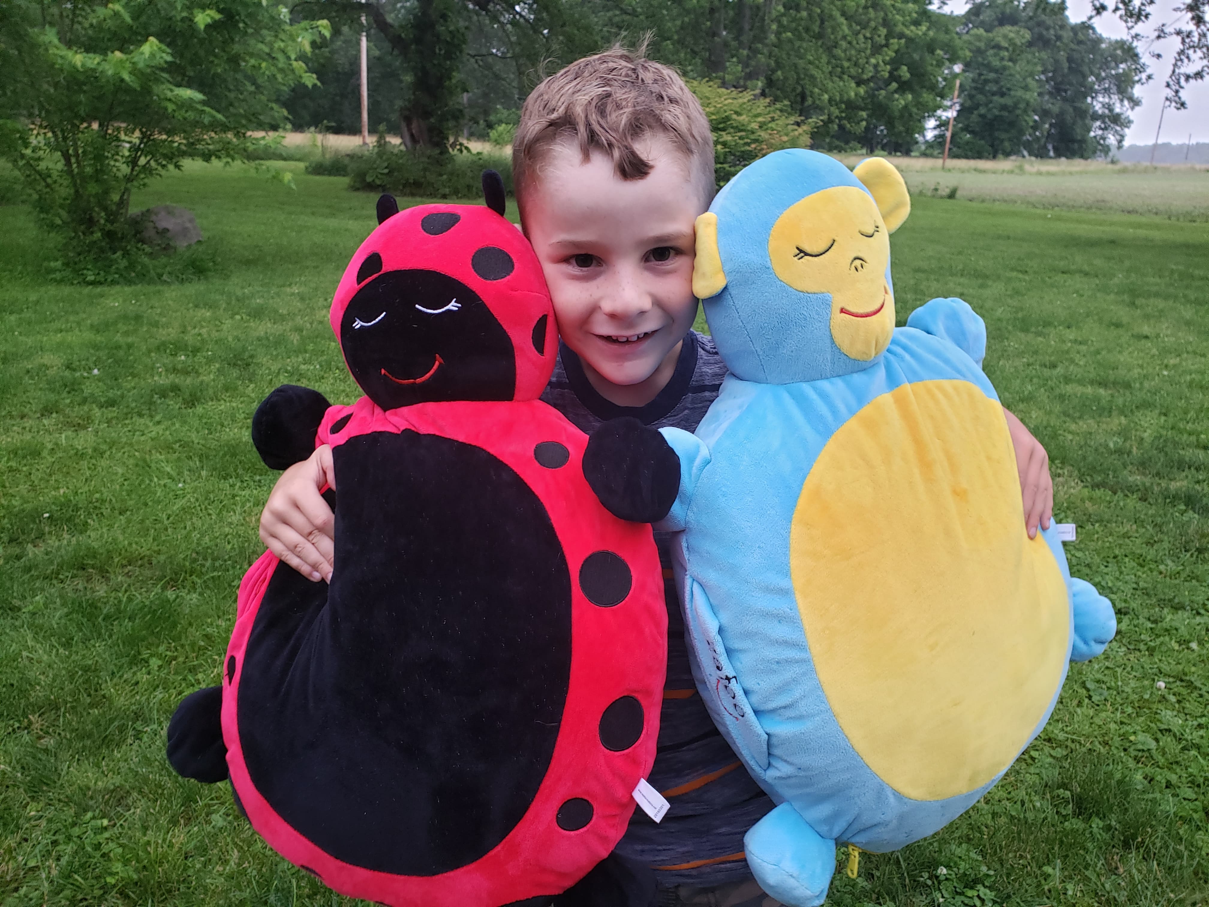 young boy hugging two large stuffed toy to his body outside