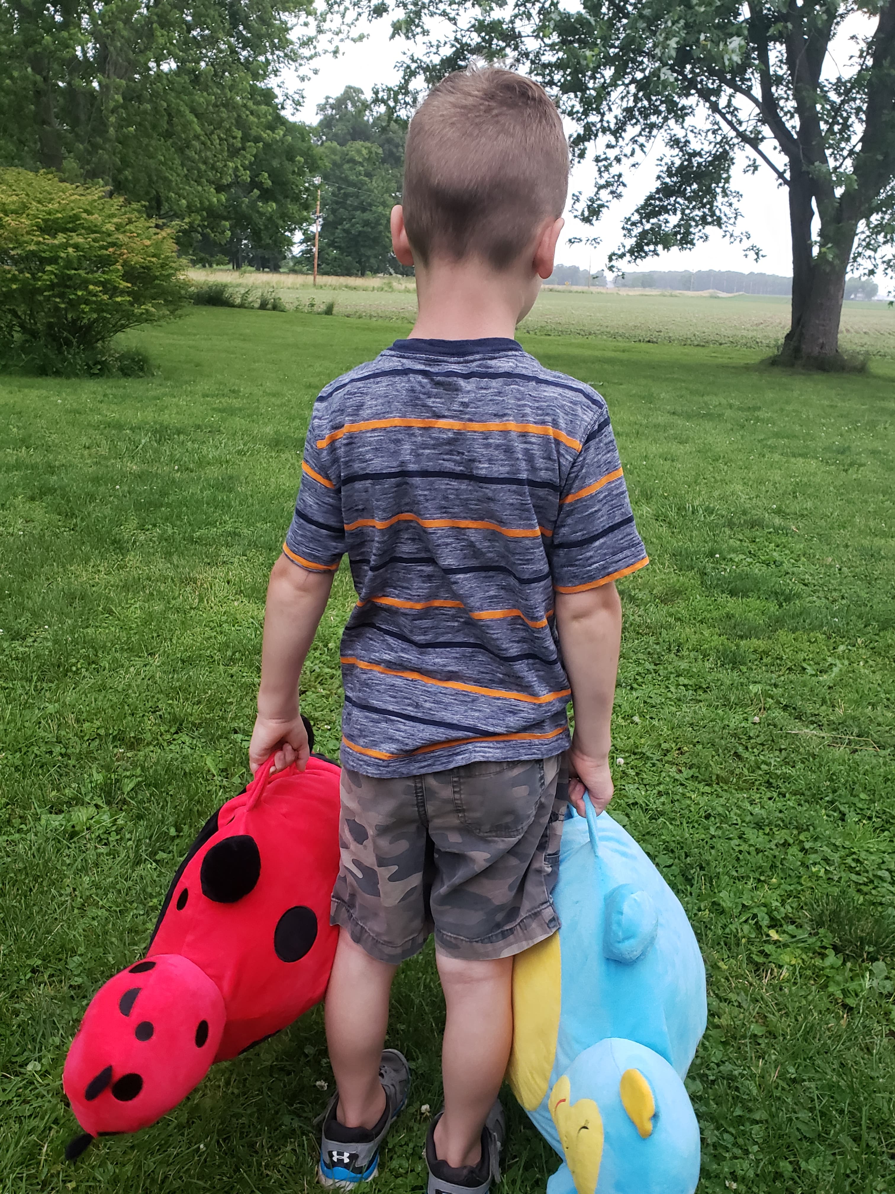 young boy carrying two large stuffed toys through a yard