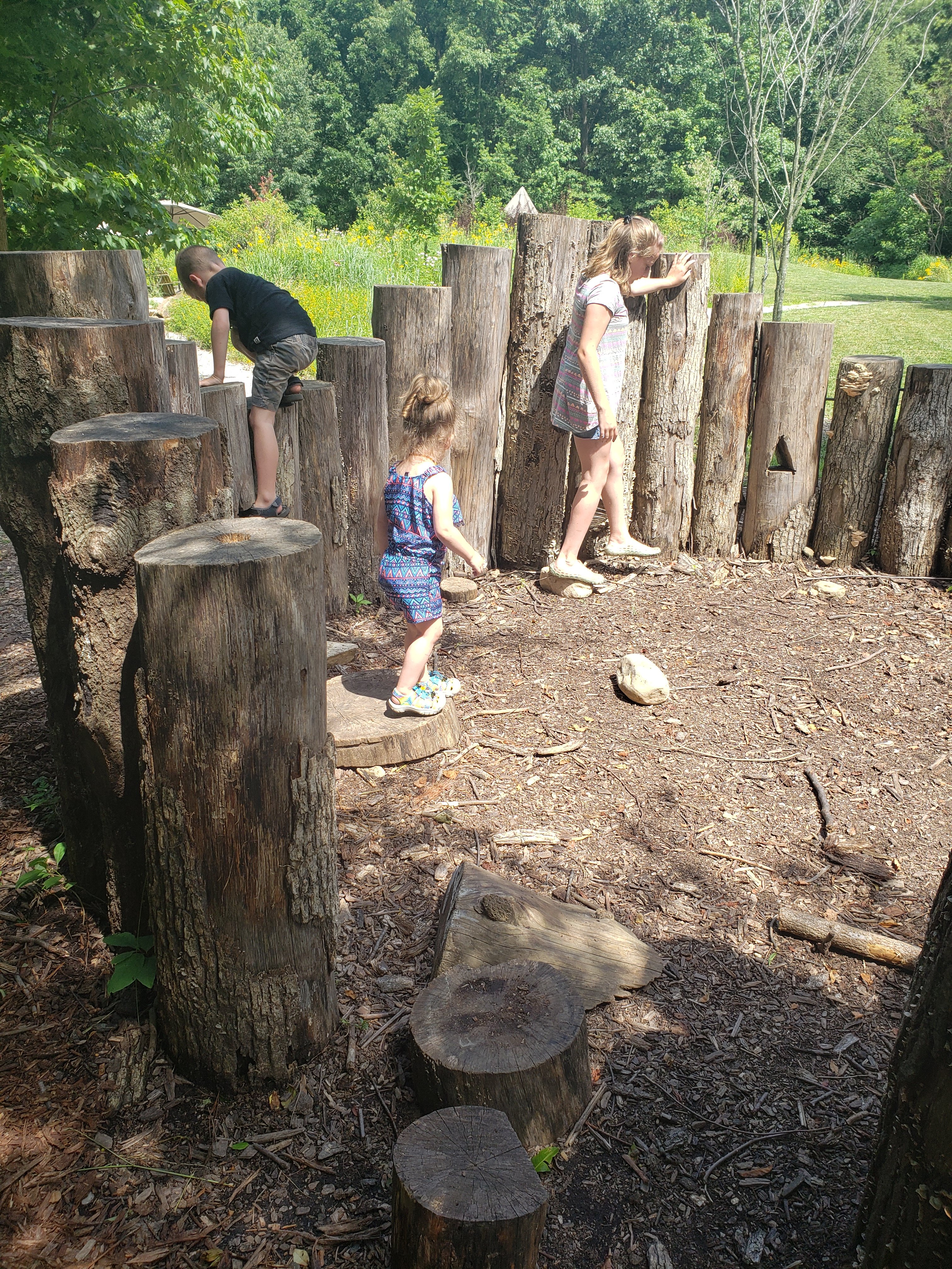 Three kids playing on large rocks at Wesselman Woods nature playscape for kids in Evansville, Indiana  Things to do with kids in Evansville Indiana. Kids activities in Evansville 