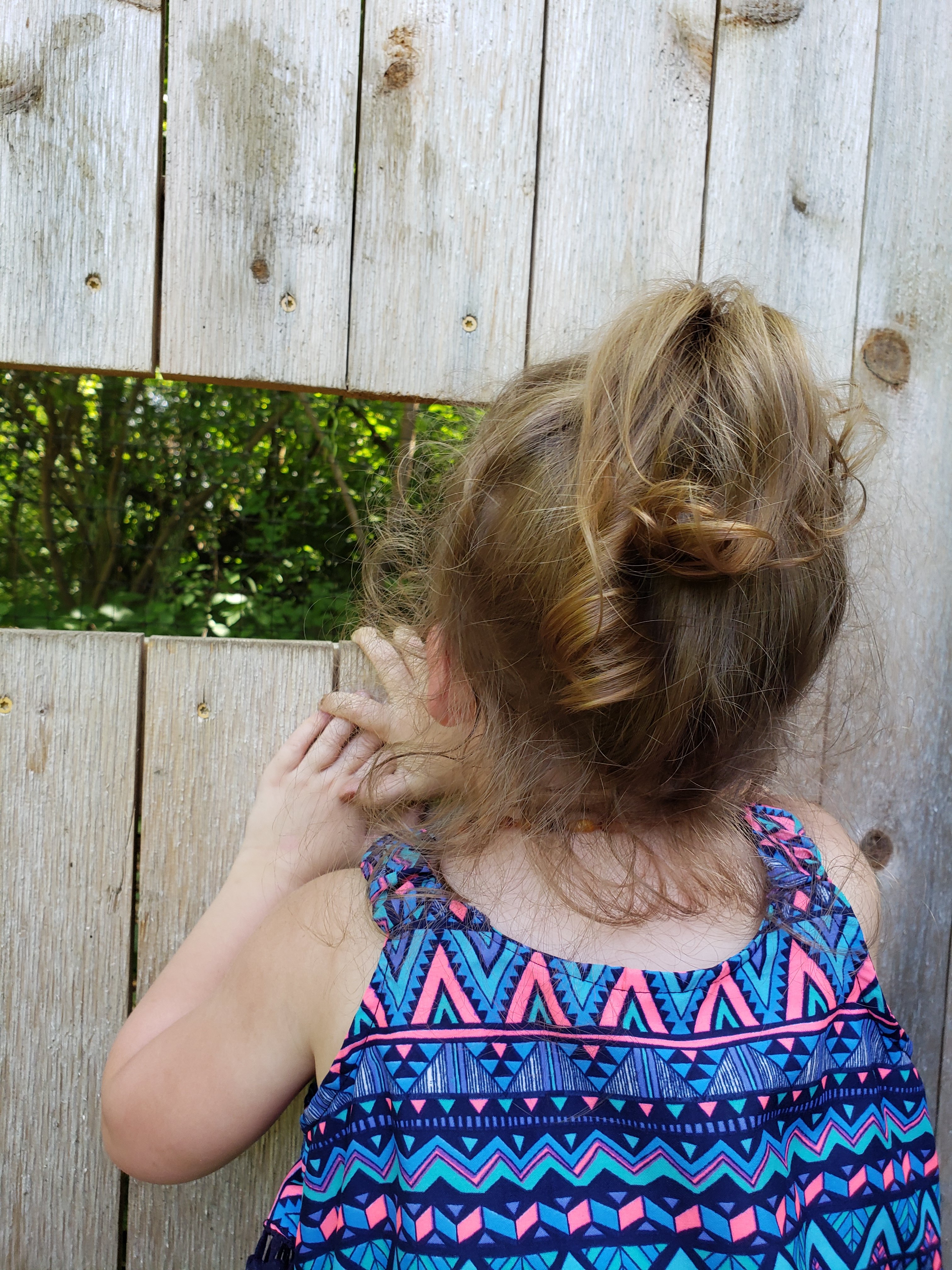 little girl peeking through a cut out in a wood fence