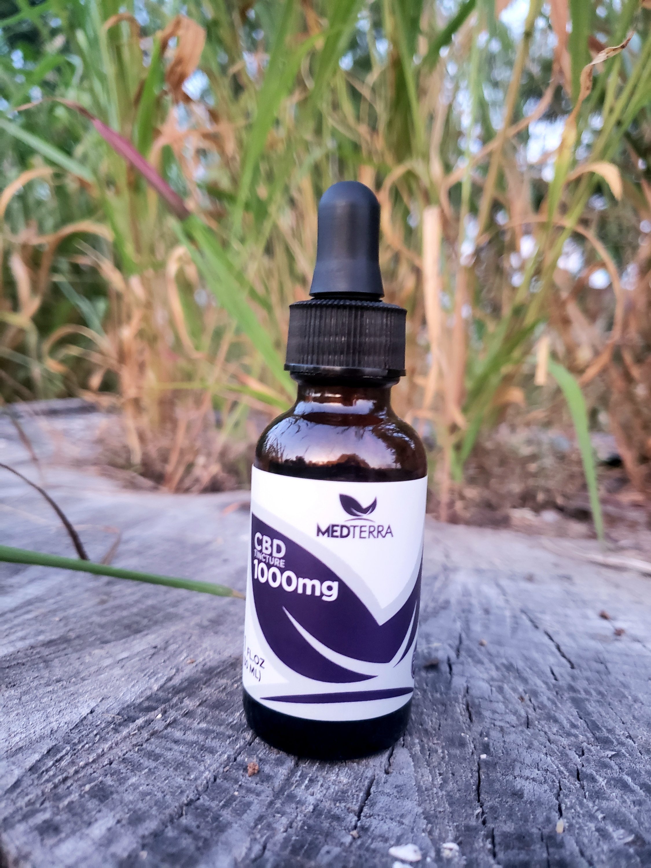 a small bottle of CBD tincture sitting on a piece of wood outside