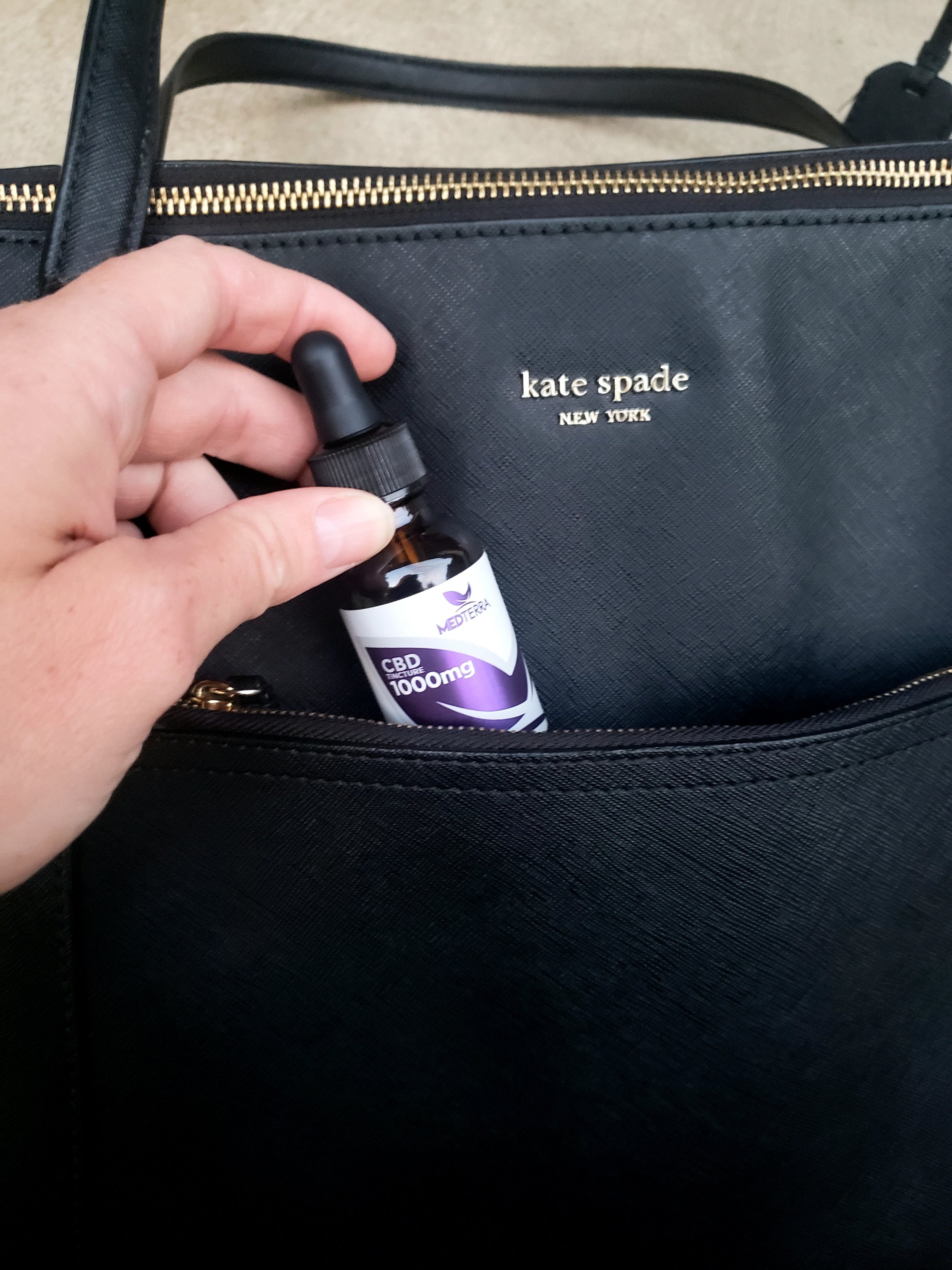 a hand slipping a small bottle of CBD tincture into a purse