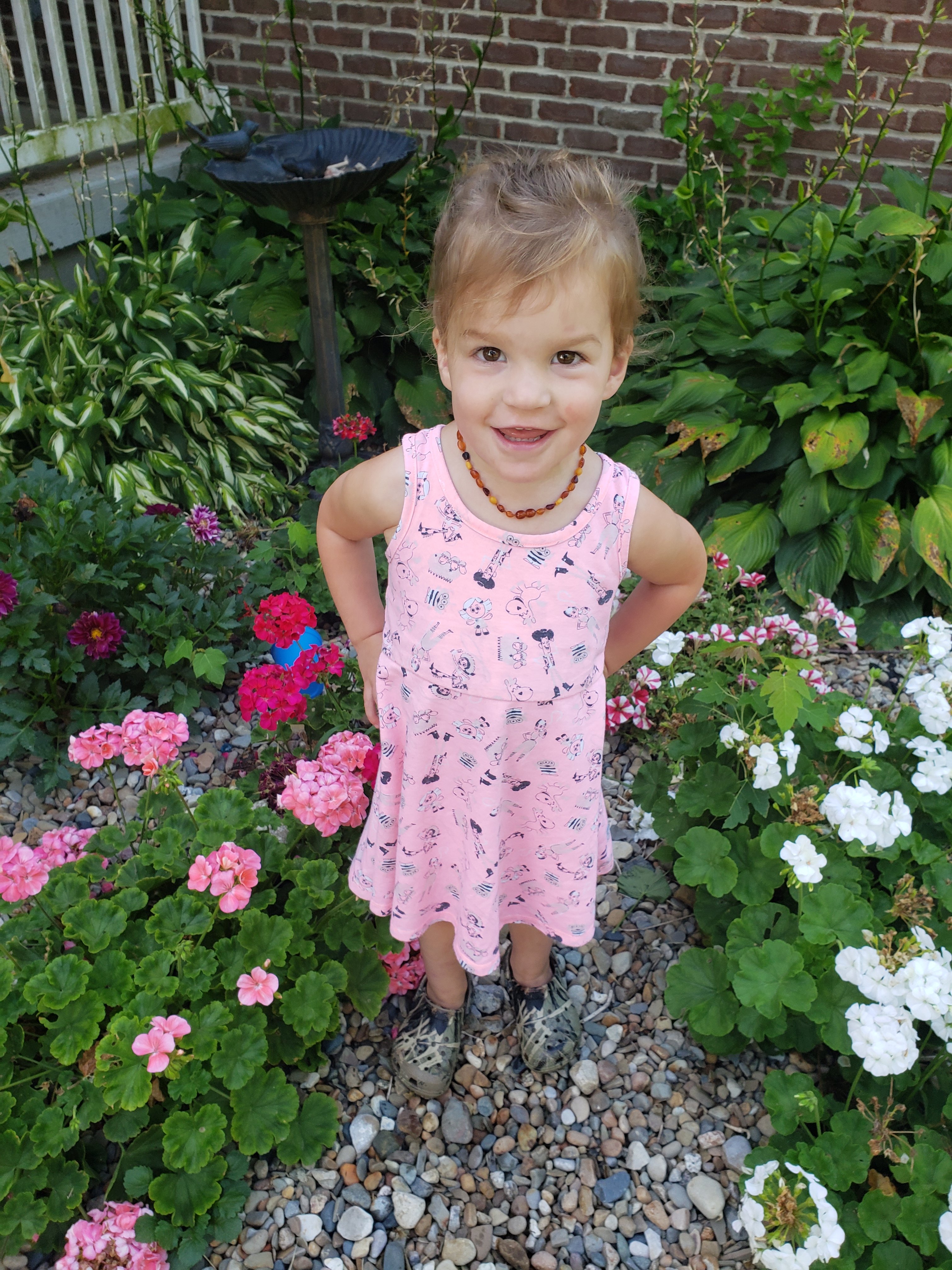 toddler standing in flower bed smiling while with her hands on her hips smiling