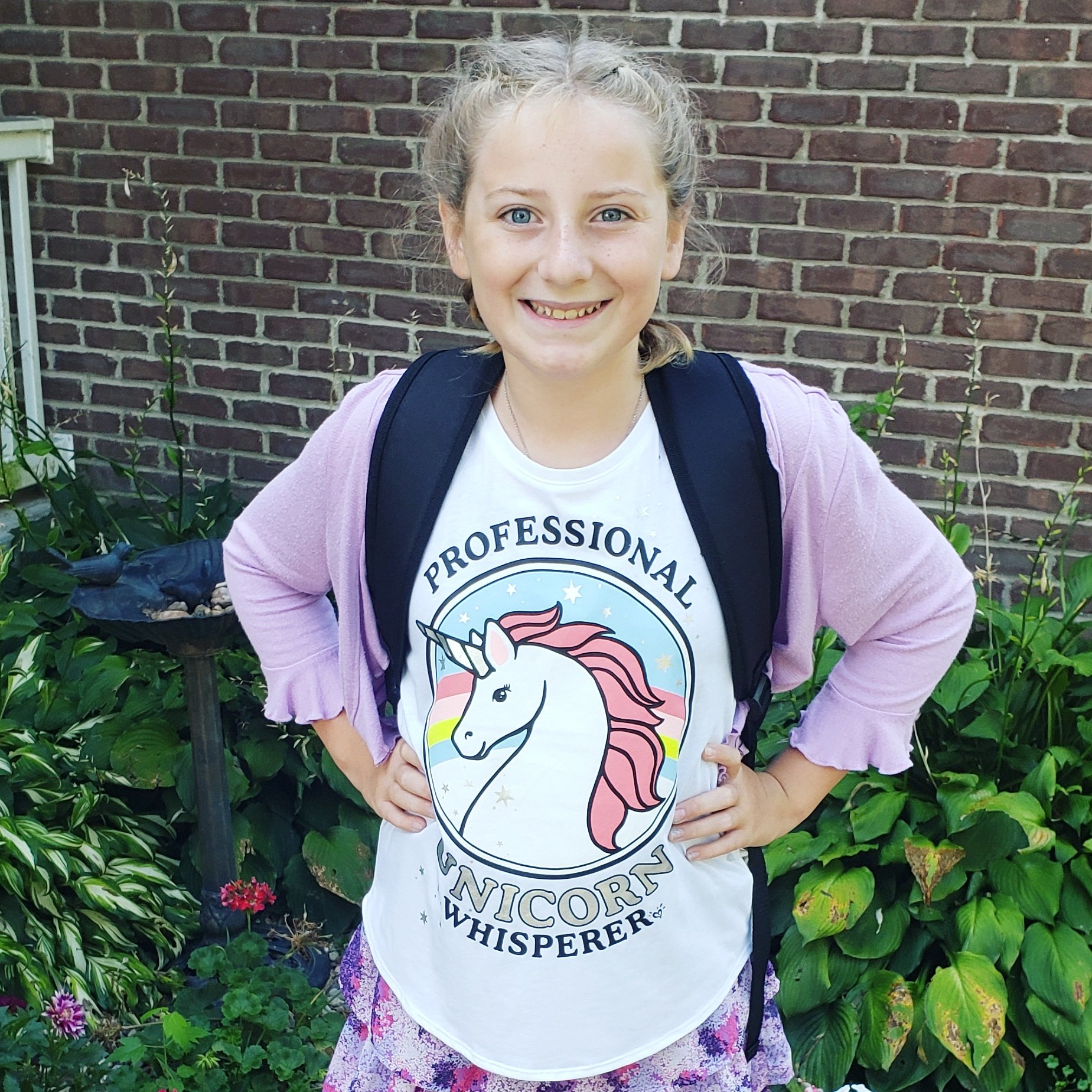 girls standing in front of a brick wall with a backpack on wearing a unicorn shirt