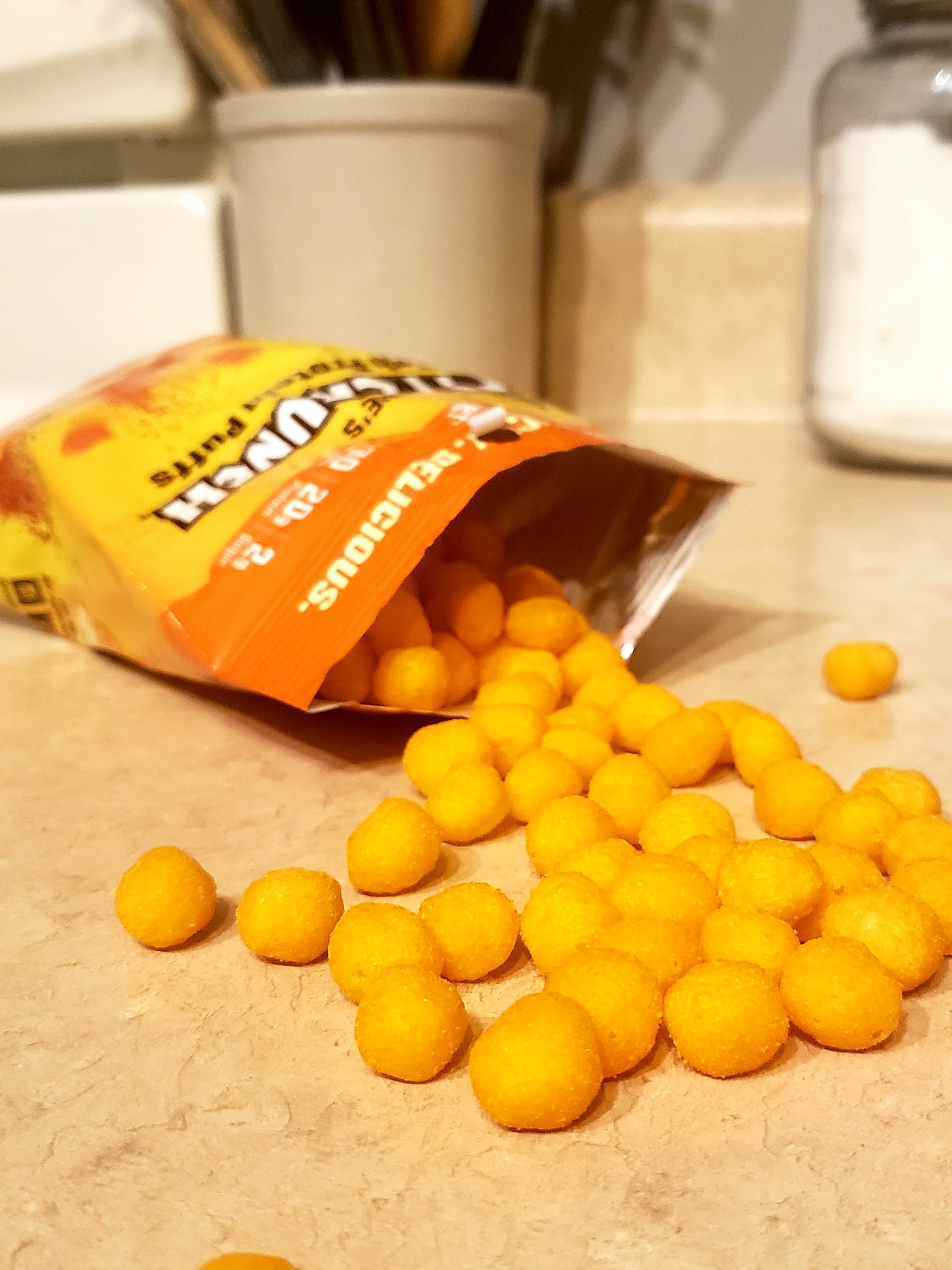 an open bag of of FitCrunch High Protein Puffs open and spilled onto a counter.