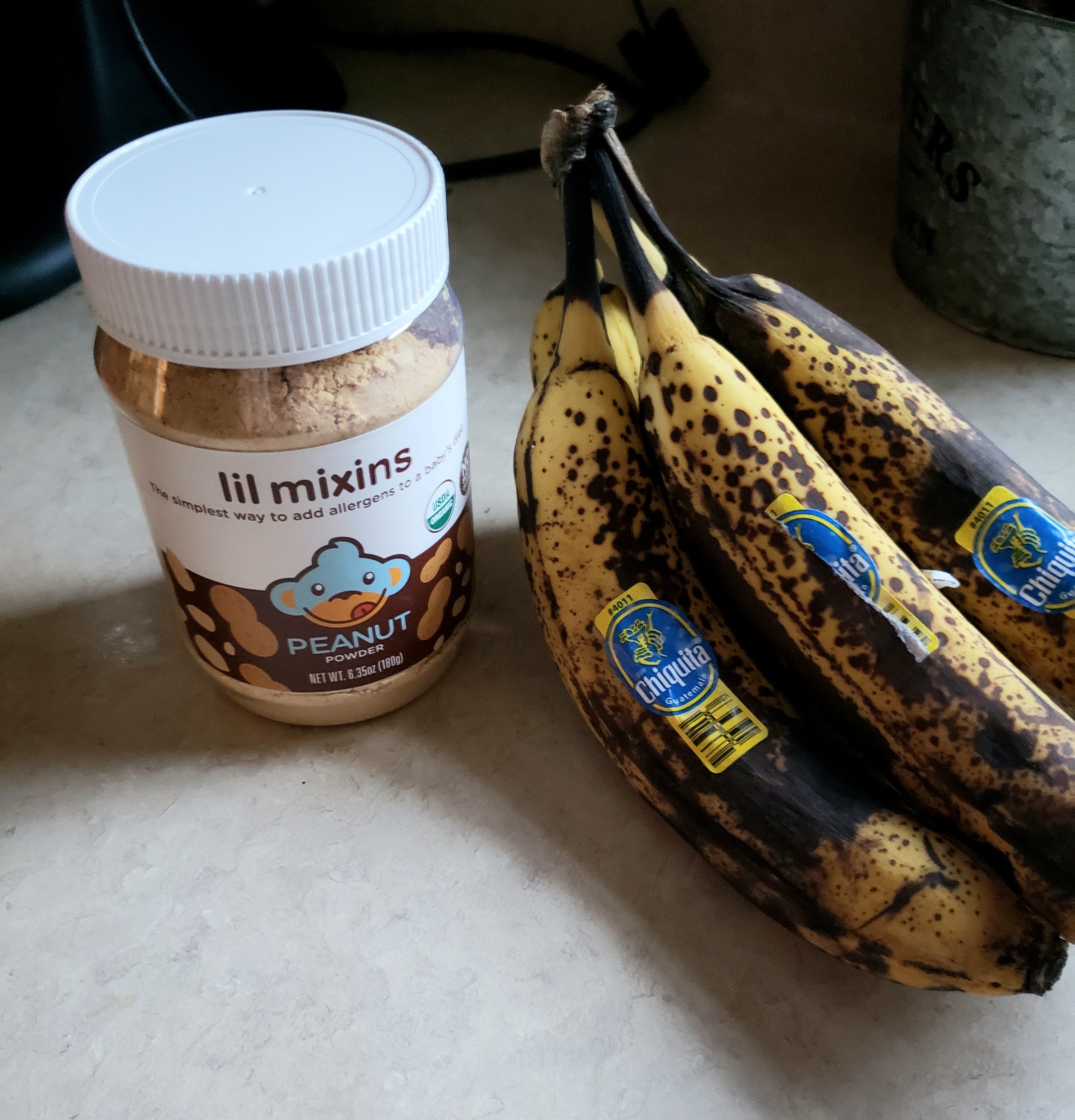 container "lil mixins" infant peanut powder next to a bunch of very ripe bananas