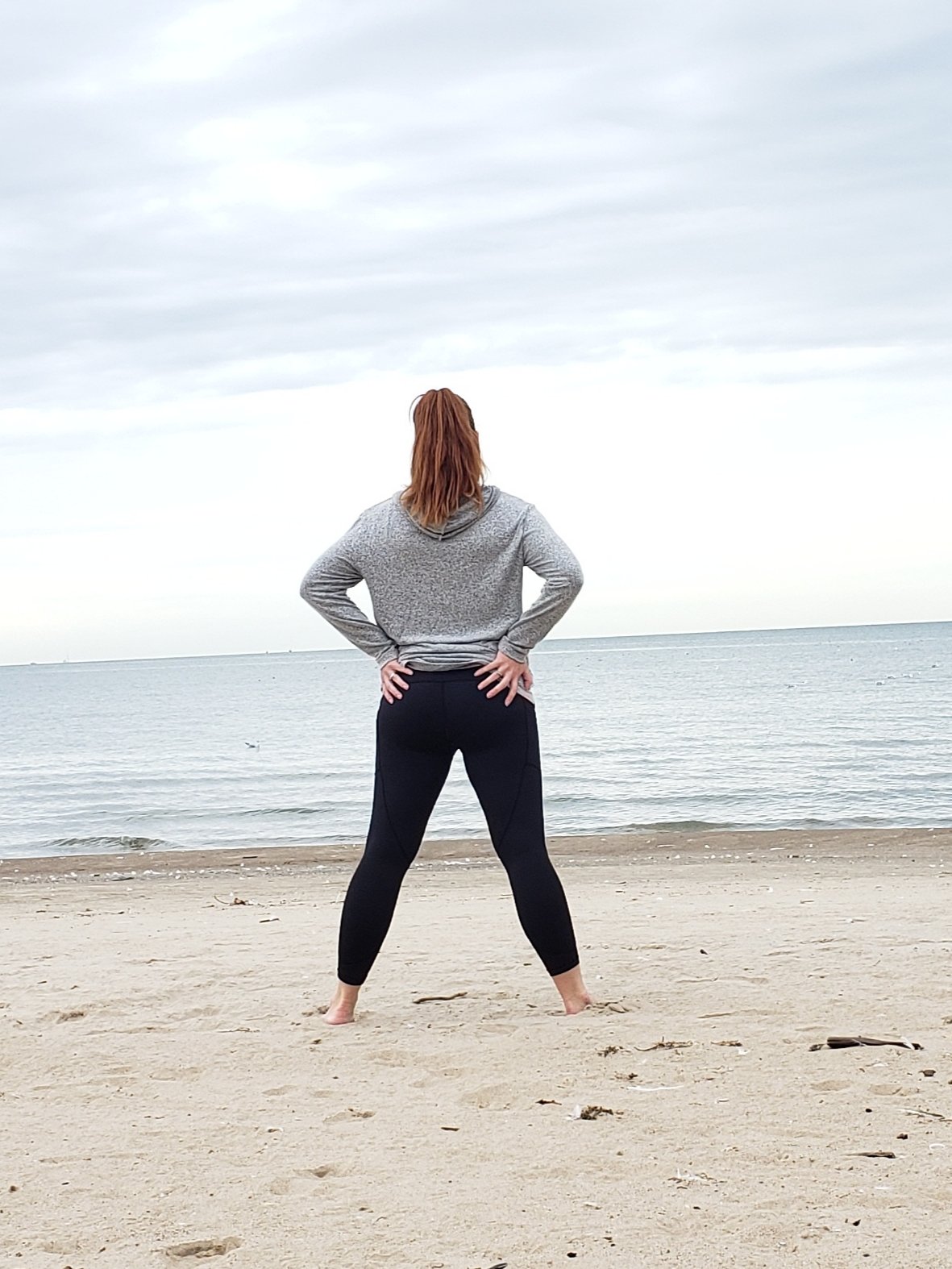 woman wearing ZYIA outfit standing wide legged on the beach with hands on hips looking out at the ocean